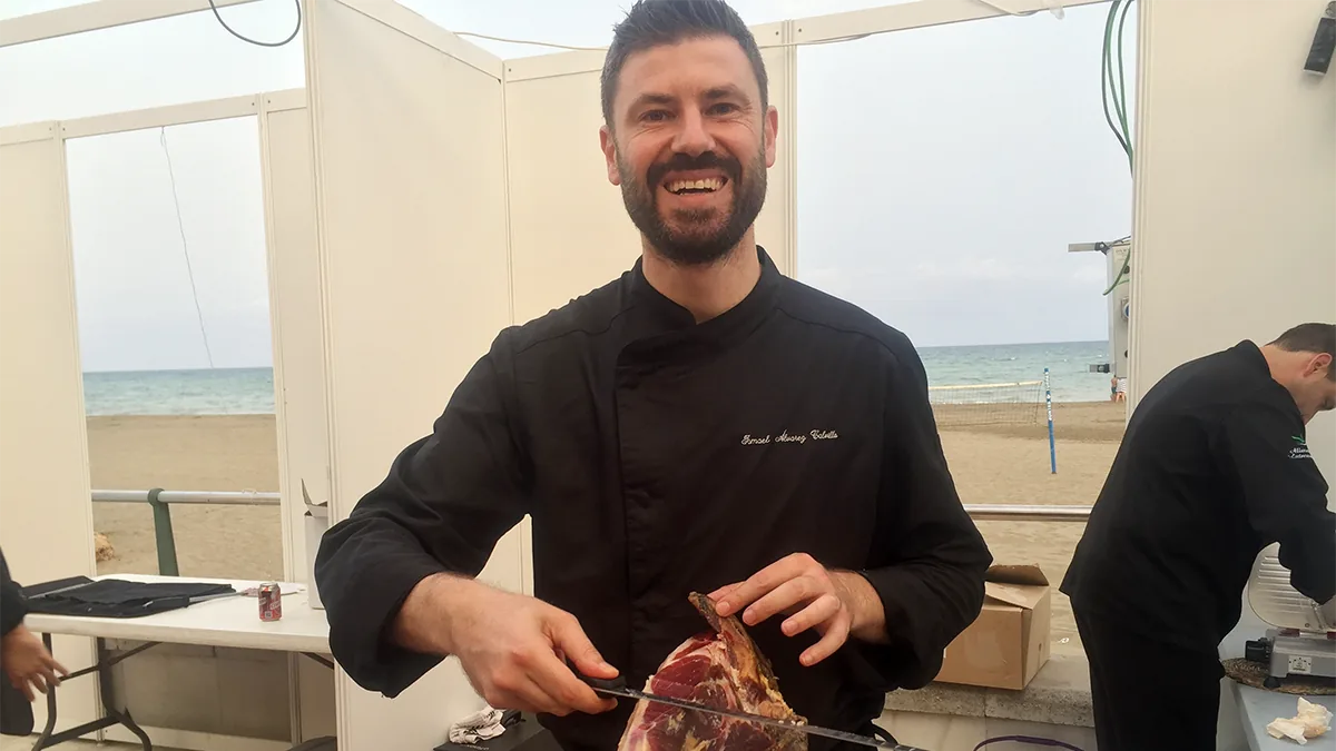 A smiling carver slices ham at his stand, with the beach behind him, 2016