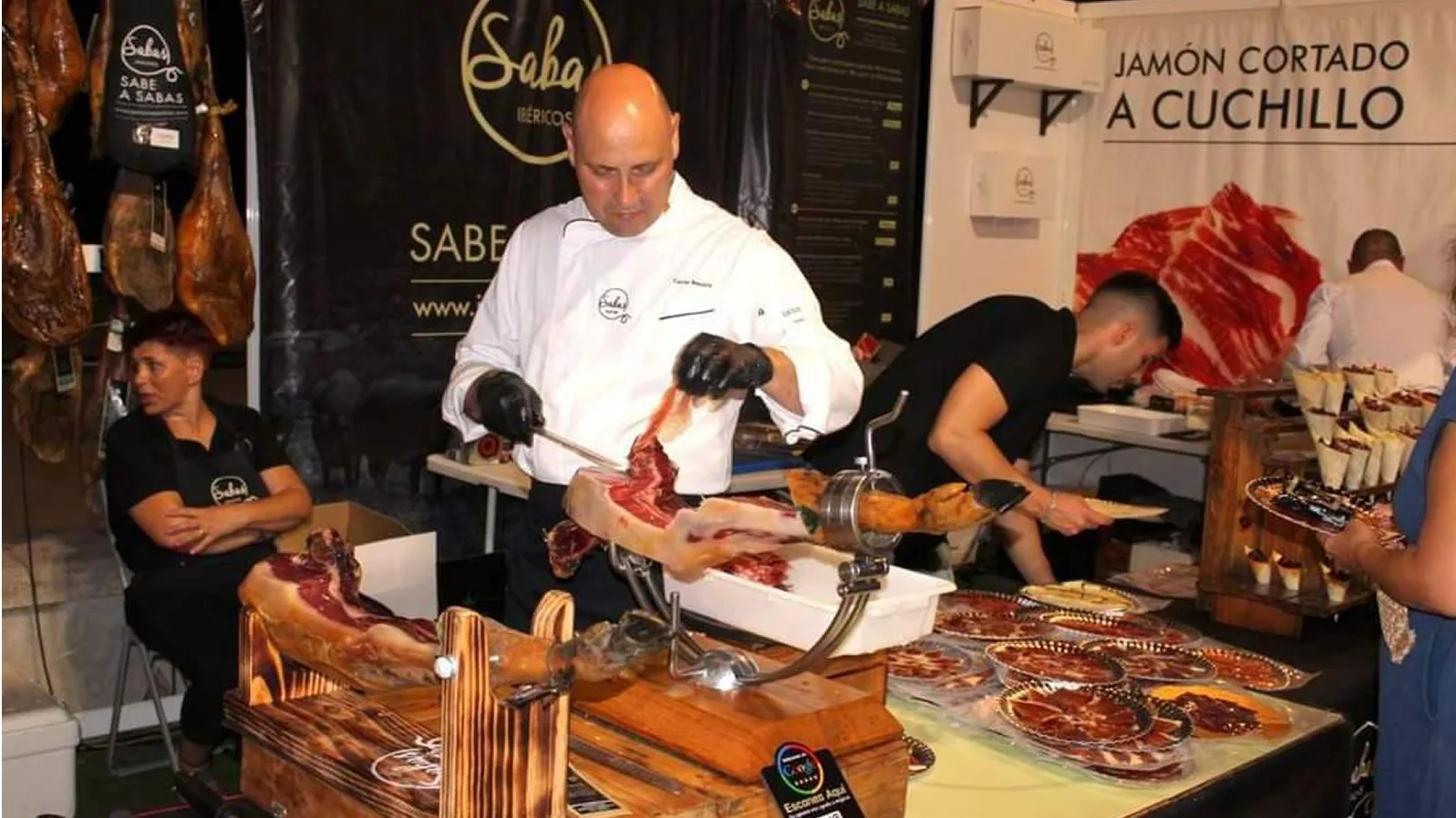 A carver in a white jacket carves ham by knife at a Certamen stand, 2022