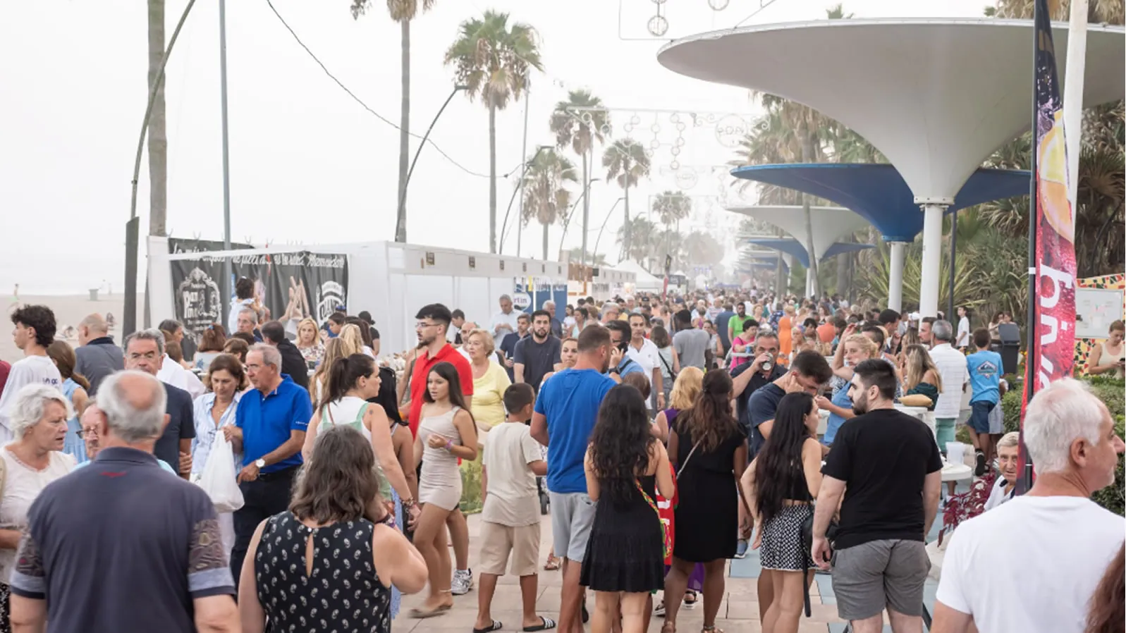 Estepona's seafront promenade packed with visitors during the World Ham Contest Popi, with palm trees and the sea behind